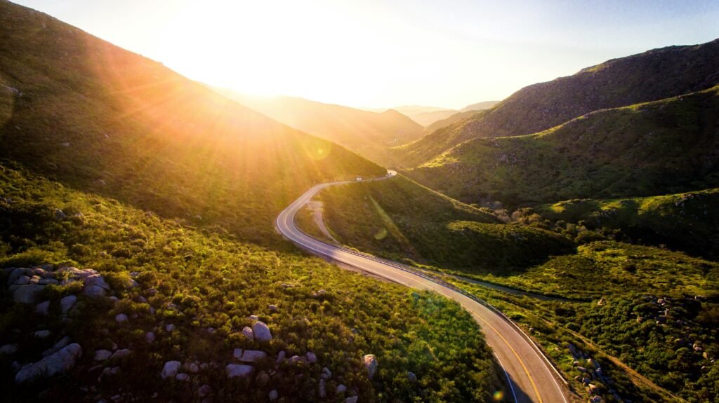 highway between hilly grassy mountains with sunrise